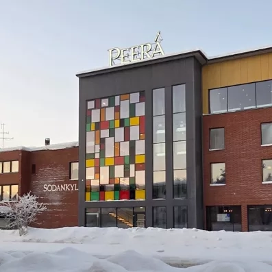 Façade extérieure de l'Hôtel Sodankylä sous la neige, bâtiment moderne avec vitraux colorés et enseigne lumineuse en Finlande.