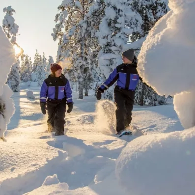 Couple profitant d'une balade en raquettes à neige dans la forêt boréale de Sodankylä au coucher du soleil.