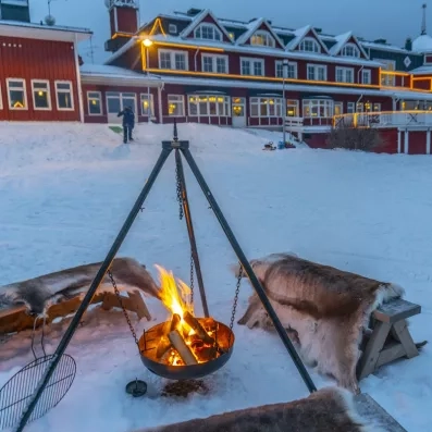 Feu de camp extérieur avec peaux de rennes devant le Grand Arctic Resort, ambiance typique Laponie.