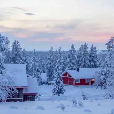 Chalets rouges typiques sous la neige au crépuscule, hébergement authentique au Grand Arctic Resort.