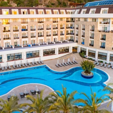 Vue de la façade de l'hôtel extérieur avec sa piscine à ses pieds et des palmiers.