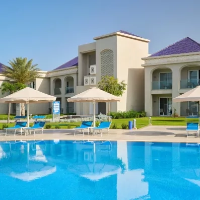 belle ambiance piscine extérieure bleue transat bleu parasol blanc et façade blanc bleu verdure