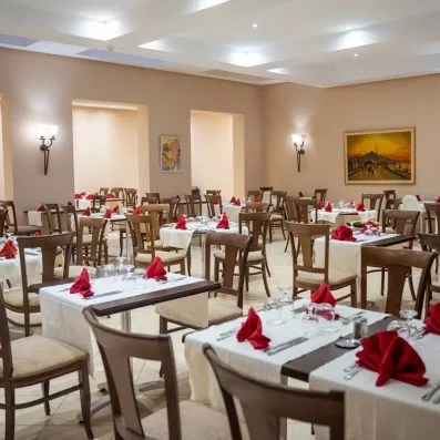 Une salle de restaurant élégante, aux tables dressées de nappes blanches et serviettes rouges, prête à accueillir les convives.