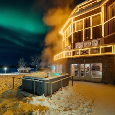 Bain à remous extérieur enneigé avec vue sur les aurores boréales au Grand Arctic Resort en Suède.