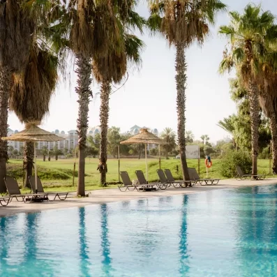 Piscine extérieure de l'hôtel Seabel Alhambra avec transats, parasols en paille et palmiers sous le soleil de Monastir, Tunisie.