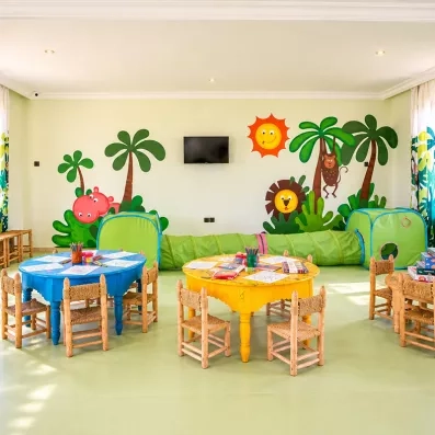 mini club enfant décoré par des palmiers au mur avec des petites tables/chaises et des jeux