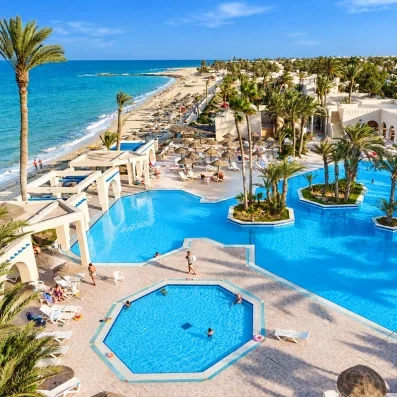 Vue aérienne du complexe hôtelier avec de grandes piscines lagon bleues, des palmiers, des transats et la plage de sable fin bordant la mer Méditerranée à Zarzis.