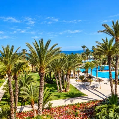 Vue panoramique sur le parc luxuriant de l'hôtel composé de nombreux palmiers, d'allées pavées et de jardins fleuris surplombant la piscine et la mer.