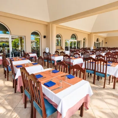Salle de restaurant intérieure de l'hôtel avec de grandes tables dressées, chaises en bois sombre et arcades architecturales typiques.