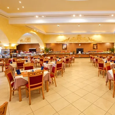 Vaste salle à manger principale de l'hôtel avec buffet central, éclairage chaleureux et décoration murale inspirée du patrimoine de Zarzis.