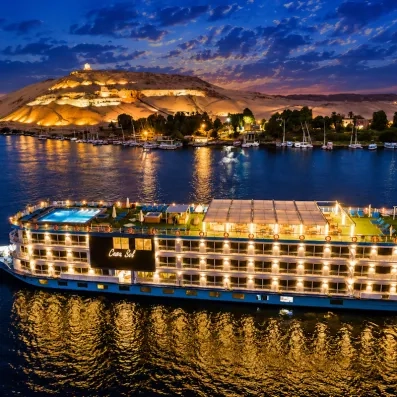 Navire illuminé de nuit sur le Nil devant des collines désertiques éclairées, croisière mer Rouge.