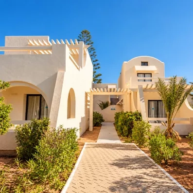 Allée pavée entre les bungalows blancs et palmiers de l'hôtel de luxe César Thalasso à Djerba.