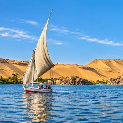 Felouque traditionnelle naviguant sur le Nil devant les dunes de sable d'Assouan, voyage authentique en Égypte.
