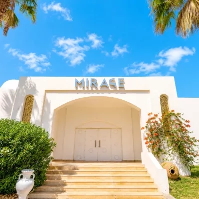 Façade blanche épurée de l'espace Mirage sous un ciel bleu radieux à l'hôtel Djerba Golf Resort.