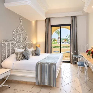 Chambre de luxe à l'hôtel Djerba Aqua Resort avec lit en fer forgé oriental et balcons vue piscine.