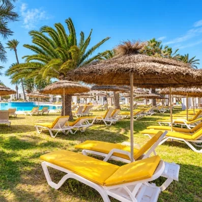 Grande piscine extérieure bordée de transats jaunes et de parasols en paille sous le soleil de Djerba.