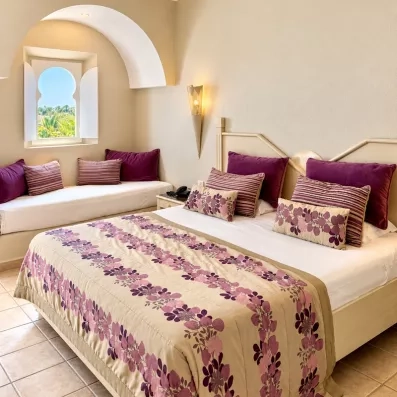 Chambre triple au Djerba Resort alliant confort moderne et architecture tunisienne avec banquette sous arche.
