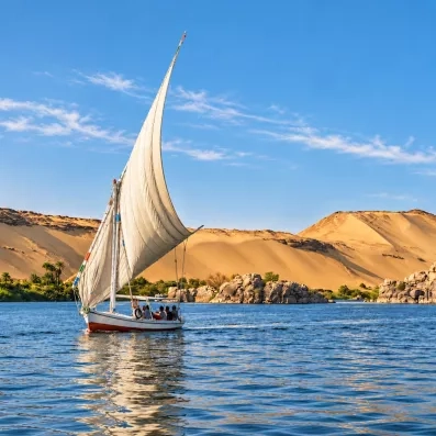 Felouque traditionnelle naviguant sur le Nil devant des dunes de sable doré, croisière Féérie du Nil.