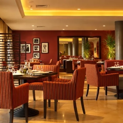 Restaurant chic Jaz Aquamarine Hurghada, dîner gastronomique en Égypte, fauteuils rayés et décoration murale élégante.