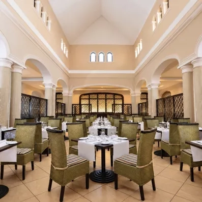 Grande salle de restaurant avec tables dressés et fauteuils en velours verts