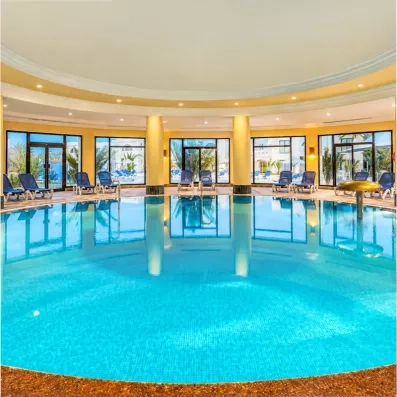 Grande piscine intérieure chauffée avec jets massants et larges baies vitrées pour se relaxer.