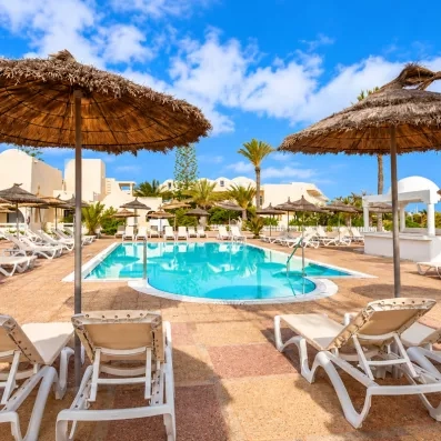 Piscine extérieure azur entourée de parasols en paille et transats pour un séjour détente à Djerba.