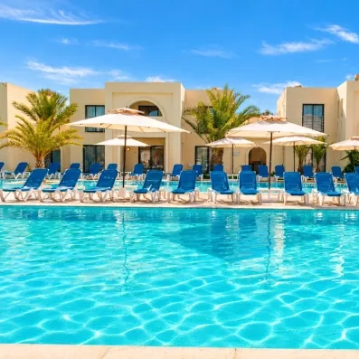 piscine turquoise avec rangée de transats et architecture tunisenne blanche et palmiers à djerba au cesar thalasso