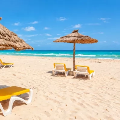 Plage de sable fin avec parasols en paille et transats jaunes au César Thalasso à Djerba.
