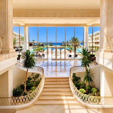 Hall de réception luxueux avec escalier monumental, grandes baies vitrées et vue sur jardin à Monastir.