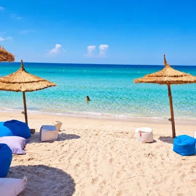 Plage de sable fin avec parasols en paille et mer turquoise au complexe hôtelier Royal Thalassa Monastir.