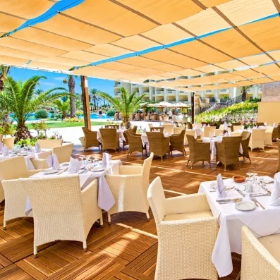 Terrasse de restaurant ombragée avec mobilier en rotin blanc près de la piscine au Royal Thalassa Monastir.