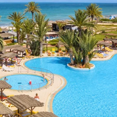 Vue sur la piscine extérieure scintillante entourée de palmiers tropicaux.