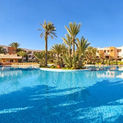 Grande piscine extérieure aux eaux cristallines entourée de palmiers sous un ciel bleu à l'hôtel Safira Palms.
