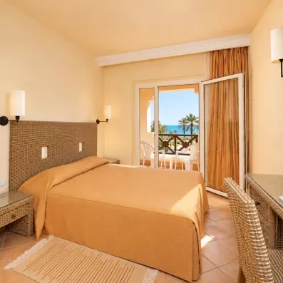 Intérieur de chambre spacieuse au Safira Palms avec bureau, tête de lit tressée et ouverture sur terrasse.