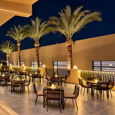 Terrasse de restaurant illuminée de nuit avec palmiers et mobilier moderne au Stella Beach, Égypte.
