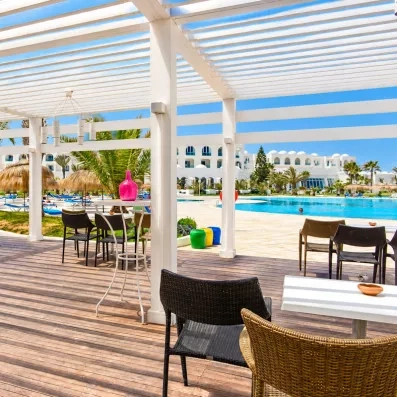 Terrasse ombragée sous une pergola blanche offrant une vue imprenable sur la piscine de l'hôtel à Djerba.