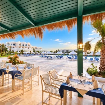 Terrasse du restaurant extérieur de l'hôtel Helios Beach avec vue sur la piscine et les jardins exotiques.