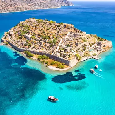 Vue aérienne de l’île de Spinalonga en Crète, forteresse vénitienne entourée d’eaux turquoise et de bateaux de plaisance.