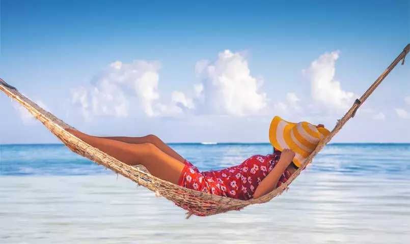 femme avec un chapeau allongée dans un hamac face à une mer turquoise en république dominicaine