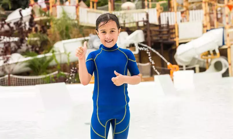 Enfant souriant dans un parc aquatique à Tenerife, toboggans et jeux d’eau en arrière-plan, activité idéale en famille aux Canaries.