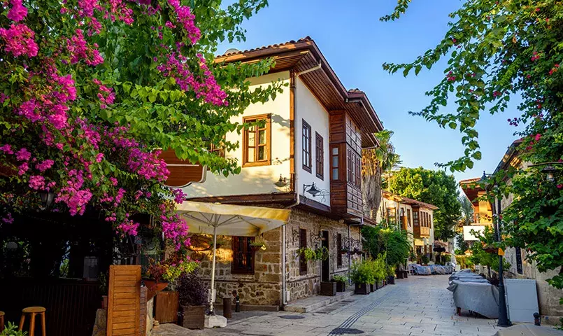 une rue en Turquie avec des maisons en bois et des bougainvilliers roses