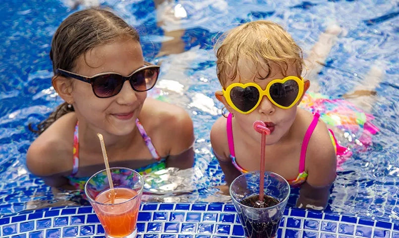 2 enfants allongés dans la piscine en buvant un jus de fruits