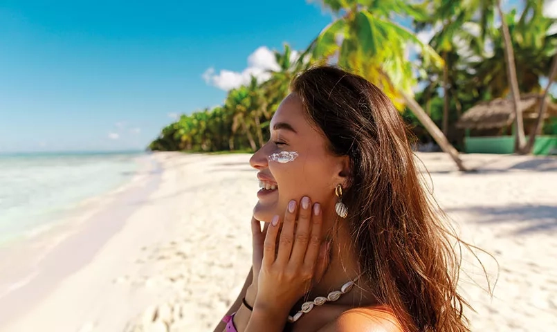 Femme se mettant de la crème solaire sur le visage sur une plage de sable blanc