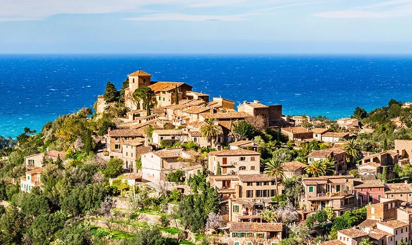 Un village s'accroche à une colline surplombant une mer d'un bleu intense.