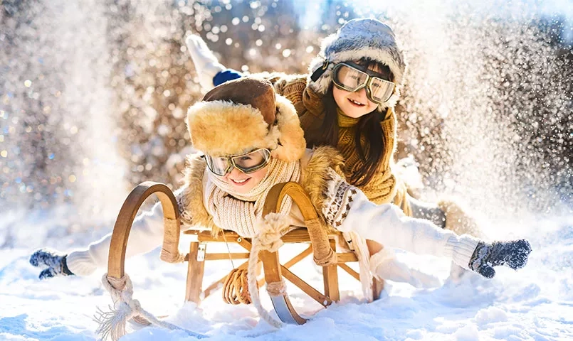 Deux enfants rient sur une luge en glissant sur la neige. 