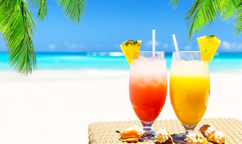Deux cocktails tropicaux colorés sur une serviette de plage, avec la mer en arrière-plan. 