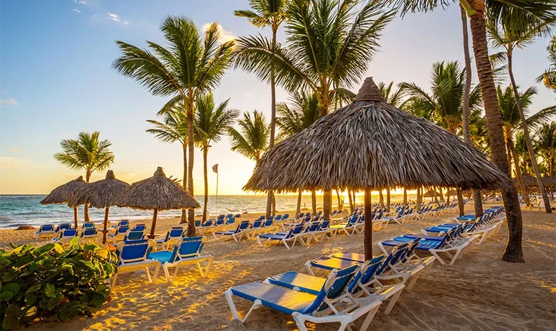 Des chaises longues et des parasols de chaume sur une plage tropicale au coucher de soleil. 