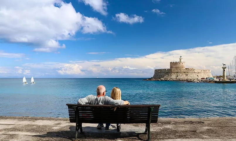 un couple de dos assis devant la ville de Rhodes