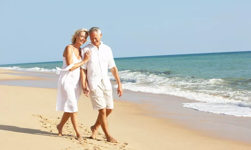 Un couple se promène main dans la main sur la plage. 
