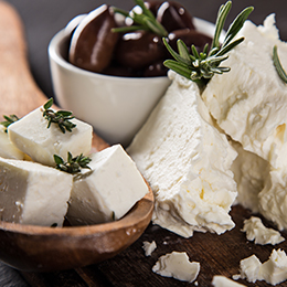 Assortiment de fromages crétois traditionnels avec olives et herbes aromatiques, spécialités grecques artisanales sur table rustique.